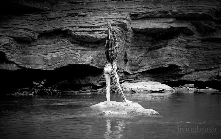 Painted model standing on a rock in a river beneath a sandstone cliff