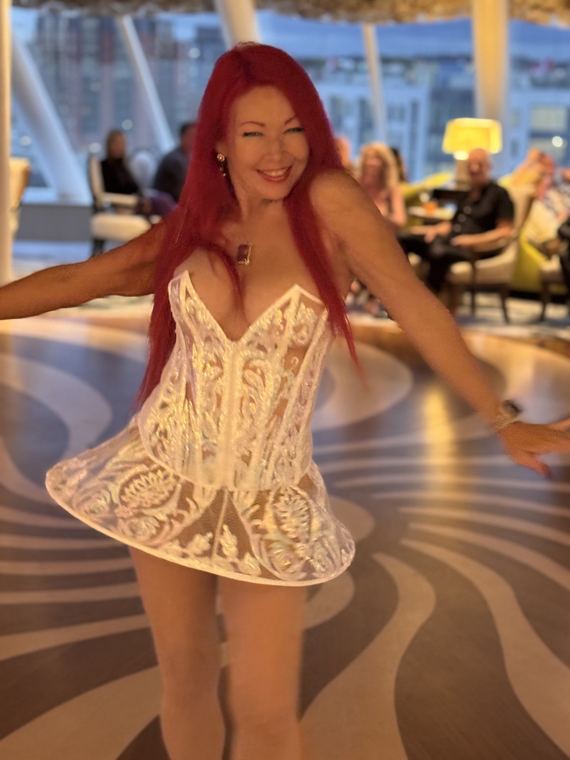 Madelyn Greco hosting in a white dress in a ship’s lounge