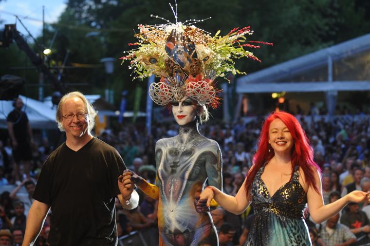 Scott and Madelyn on stage beside a painted model in a large headdress